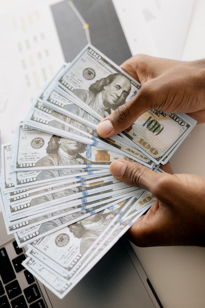 Services Close-up view of hands counting U.S. hundred dollar bills over a laptop background.