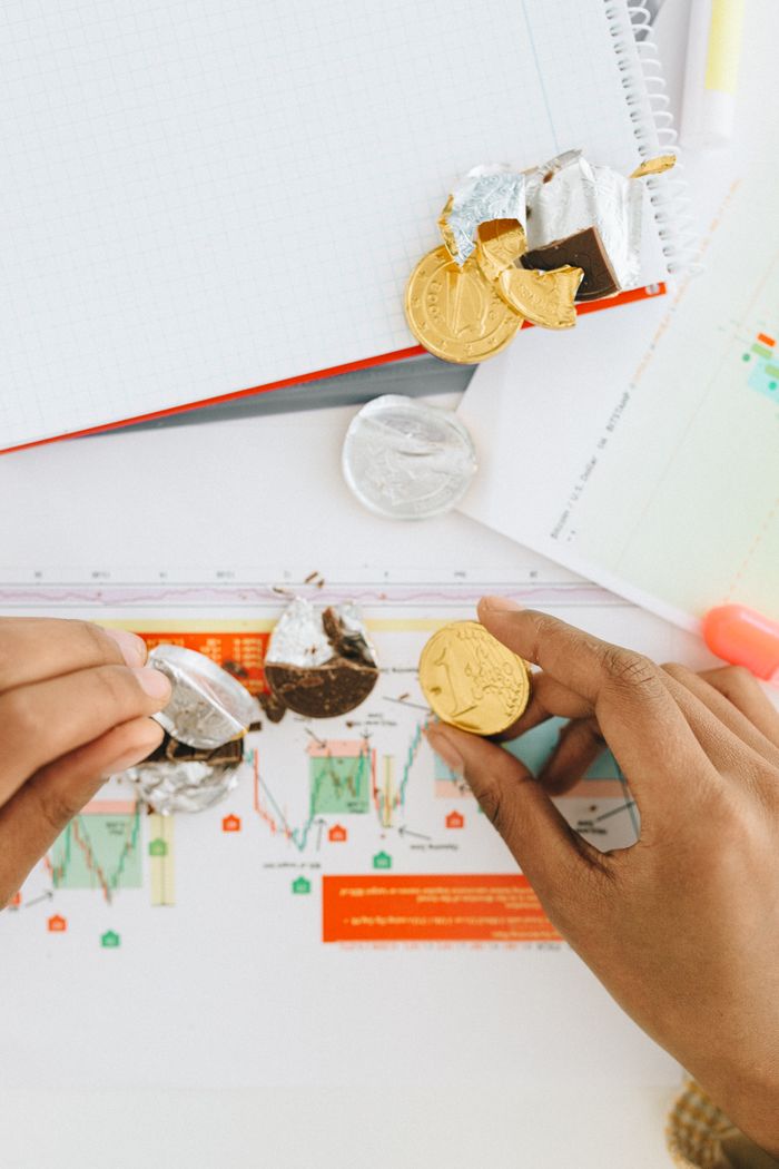 Services Close-up of hands peeling chocolate coins over financial graphs, symbolizing finance and investment.