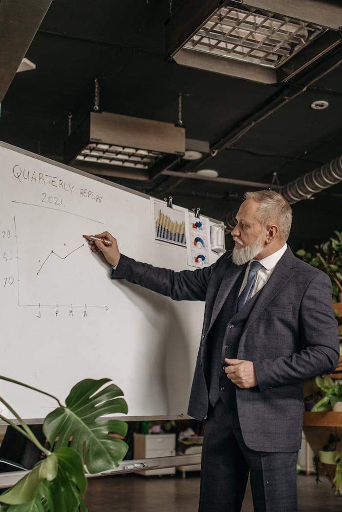 Senior executive presenting a quarterly financial report on a whiteboard in an office setting.